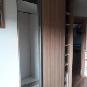 Vstavaná skriňa na mieru s posuvnými dverami v drevodekore, úložnými policami a priestorom na zavesenie oblečenia.